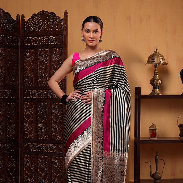 A woman posing in a traditional Fuchsia Majesty satin silk saree featuring bold black and white stripes and a vibrant fuchsia pink border, styled with a matching heavy-weave Zari blouse.