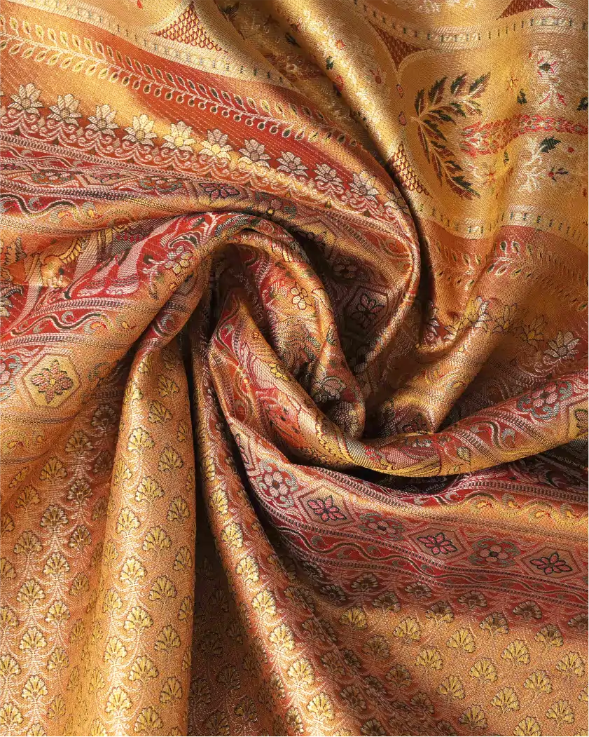Close-up swirled drape of a handwoven gold and red Kanchipuram silk saree showing intricate floral zari motifs and metallic luster.