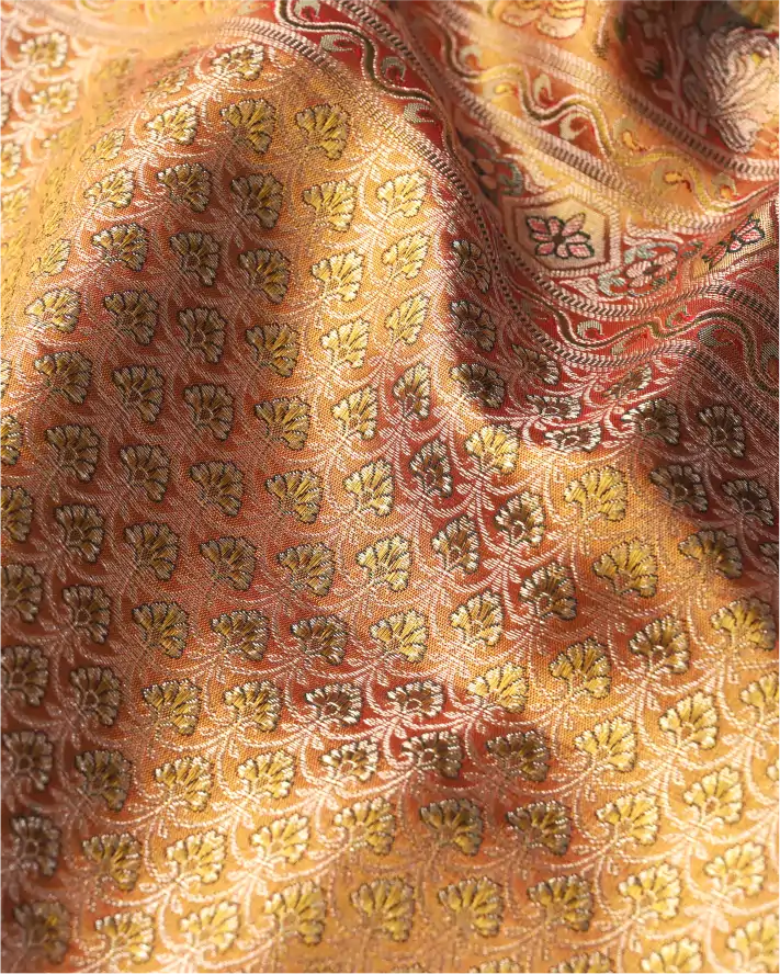 Macro close-up shot of a handwoven gold and red Kanchipuram silk saree showing intricate golden zari motifs and floral weave texture.