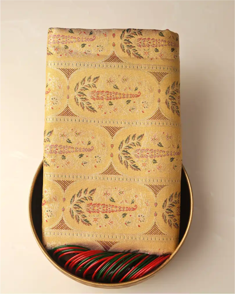 Folded golden Kanchipuram silk saree with intricate floral zari motifs displayed neatly inside a golden round tray