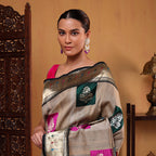 A woman posing against a wooden screen, elegantly draped in a golden beige pure Tussar silk saree with multicolored zari bootas and a heavy border.