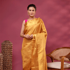 A woman posing against a dusty pink background, elegantly draped in a golden mustard yellow Kanjivaram silk saree with intricate resham zari work, paired with a vibrant pink sleeveless blouse.