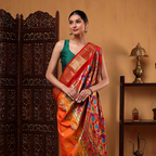 A woman posing in a handwoven Golden Sunset Paithani silk saree featuring rich mustard yellow and vibrant red colors with intricate traditional motifs, styled with a contrasting green sleeveless blouse.
