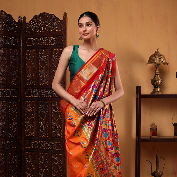 A woman posing in a handwoven Golden Sunset Paithani silk saree featuring rich mustard yellow and vibrant red colors with intricate traditional motifs, styled with a contrasting green sleeveless blouse.