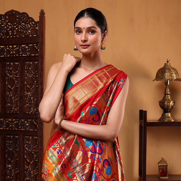 Side profile of a woman modeling the rich mustard yellow and red Paithani silk saree next to an ornate dark wooden screen partition.
