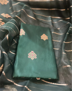 A close-up view of a premium green pure Banarasi silk suit fabric featuring intricate gold weaving, paired with a matching sheer Kora dupatta.