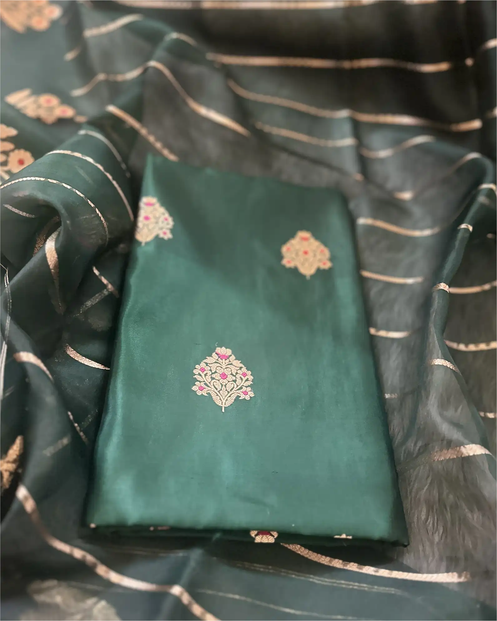 A close-up view of a premium green pure Banarasi silk suit fabric featuring intricate gold weaving, paired with a matching sheer Kora dupatta.