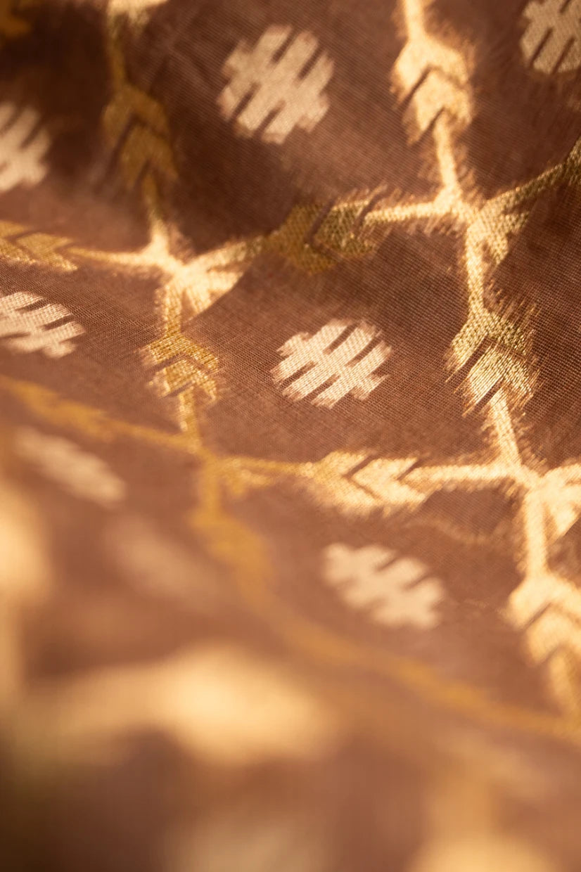 Detailed view of the handwoven gold zari motifs on an earthy brown Jamdani silk cotton saree, highlighting the fine texture and traditional craftsmanship.