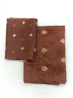 Chocolate brown handwoven Banarasi silk dupatta featuring gold zari borders and starburst motifs draped alongside folded suit fabric on a wooden hanger, set against an ornate gold mirror