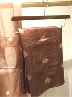 Chocolate brown handwoven Banarasi raw silk suit fabric with gold zari bootis folded on a wooden hanger, paired with a sheer Kora silk dupatta featuring starburst motifs