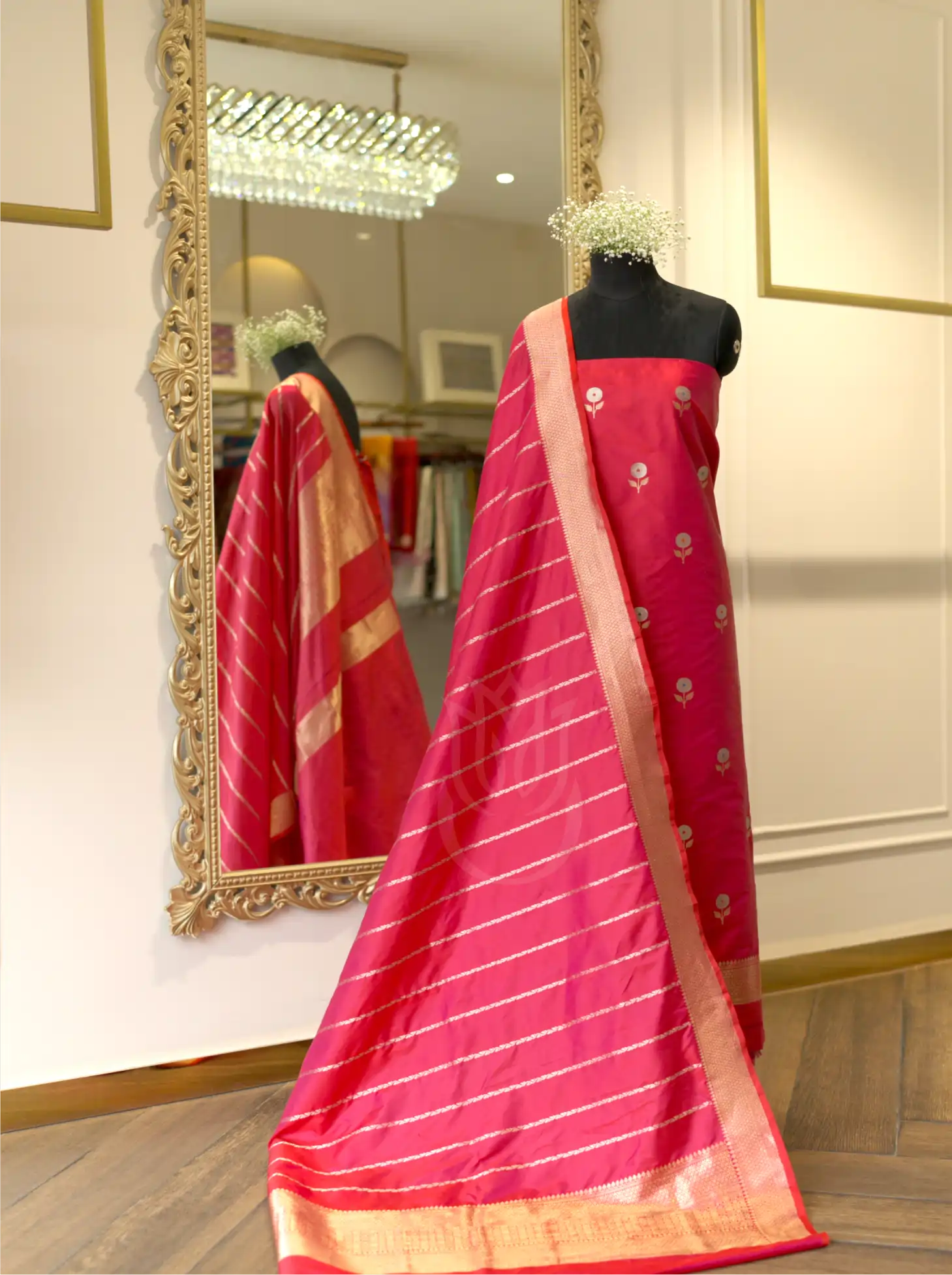 Magenta pink handwoven Banarasi silk suit set displayed on a mannequin, featuring silver floral bootis, a striped gold zari tissue dupatta with a woven border, and a large ornate gold mirror in the background.