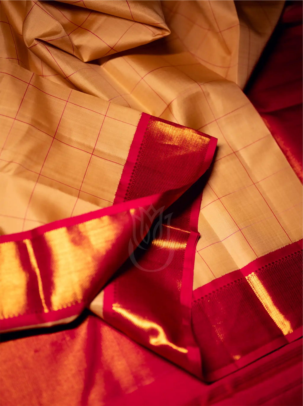 Close-up view of a handwoven beige silk saree featuring fine golden grid lines, elegantly draped with a bold crimson red zari border and rich gold pallu edge.