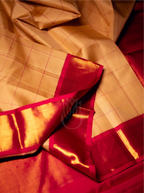 Close-up view of a handwoven beige silk saree featuring fine golden grid lines, elegantly draped with a bold crimson red zari border and rich gold pallu edge.