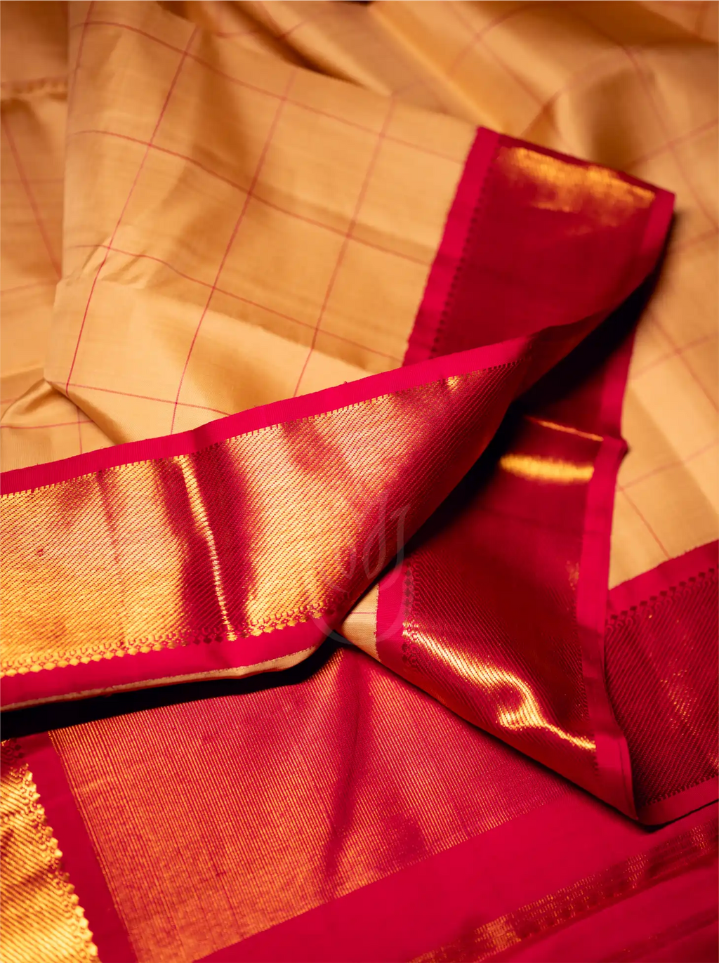 Close-up detail of a handwoven beige silk saree featuring a fine golden-yellow checked pattern, draped with a contrasting rich crimson red border and metallic gold zari pallu.