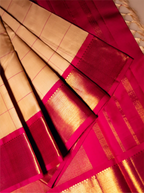 Close-up view of a folded handwoven silk saree featuring a beige checked body with shimmering gold zari lines and a contrasting vibrant magenta-pink border with metallic gold zari weave.