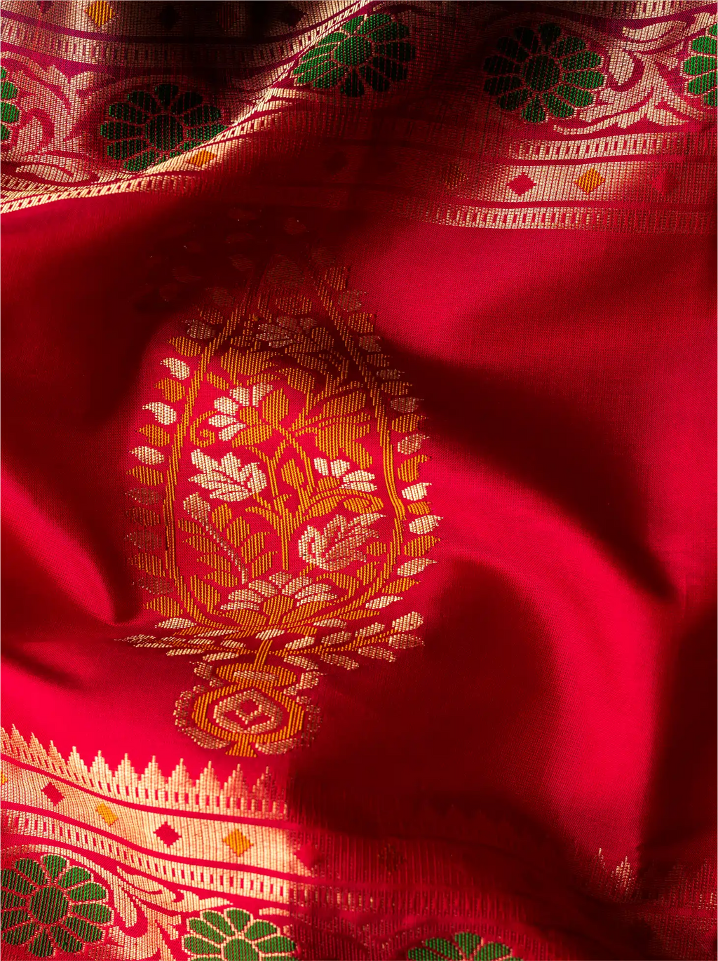 Vibrant close-up shot of a handwoven pure Paithani silk saree featuring a rich crimson red silk pallu highlighted with an intricate golden zari paisley design and colorful floral handloom borders.