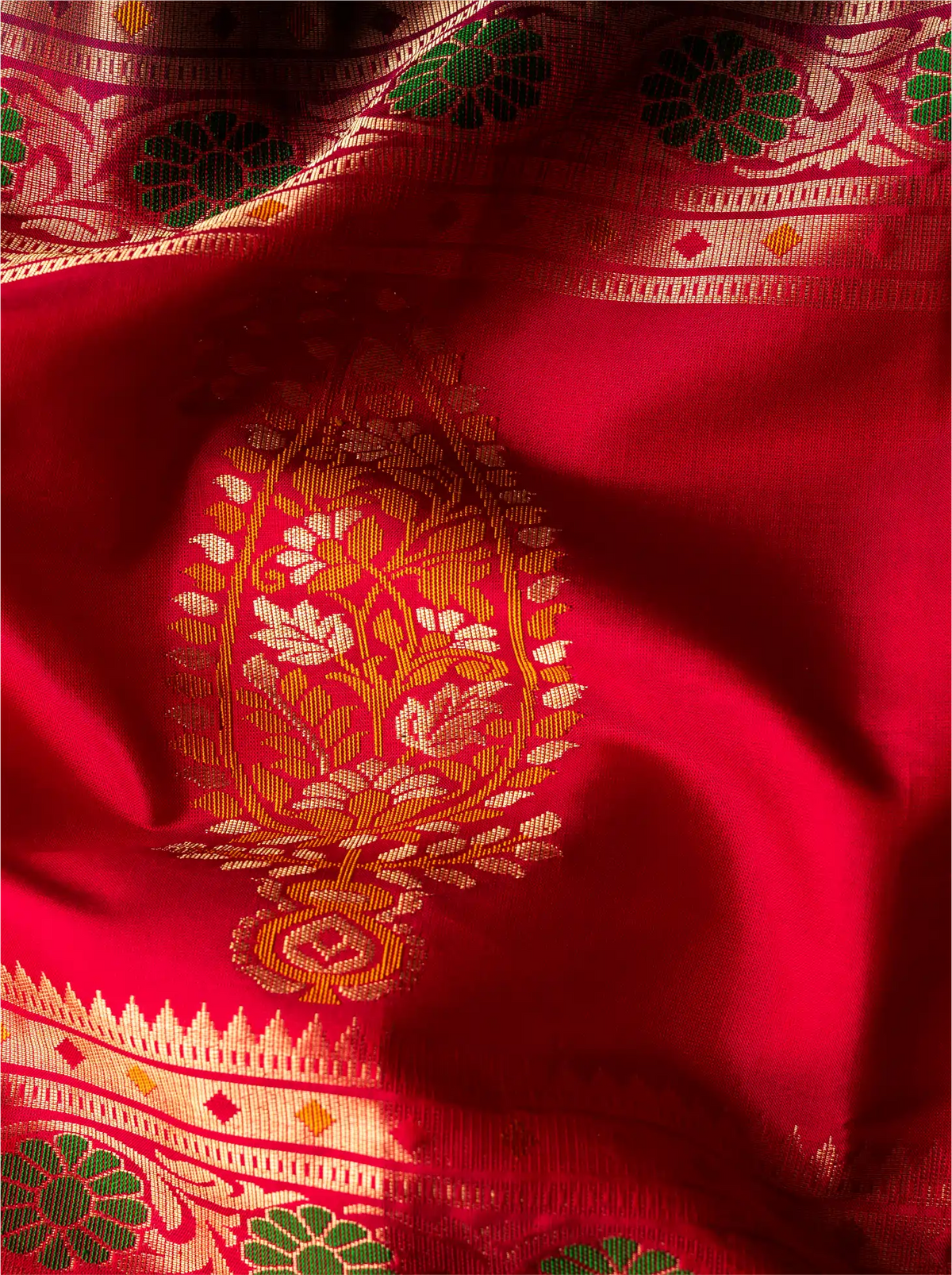 Vibrant close-up shot of a handwoven pure Paithani silk saree featuring a rich crimson red silk pallu highlighted with an intricate golden zari paisley design and colorful floral handloom borders.