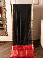 Black handwoven pure Paithani silk saree draped on a display stand, featuring gold zari buttis, thin gold borders, and a rich crimson red pallu detailed with woven peacock and floral paisley zari motifs.