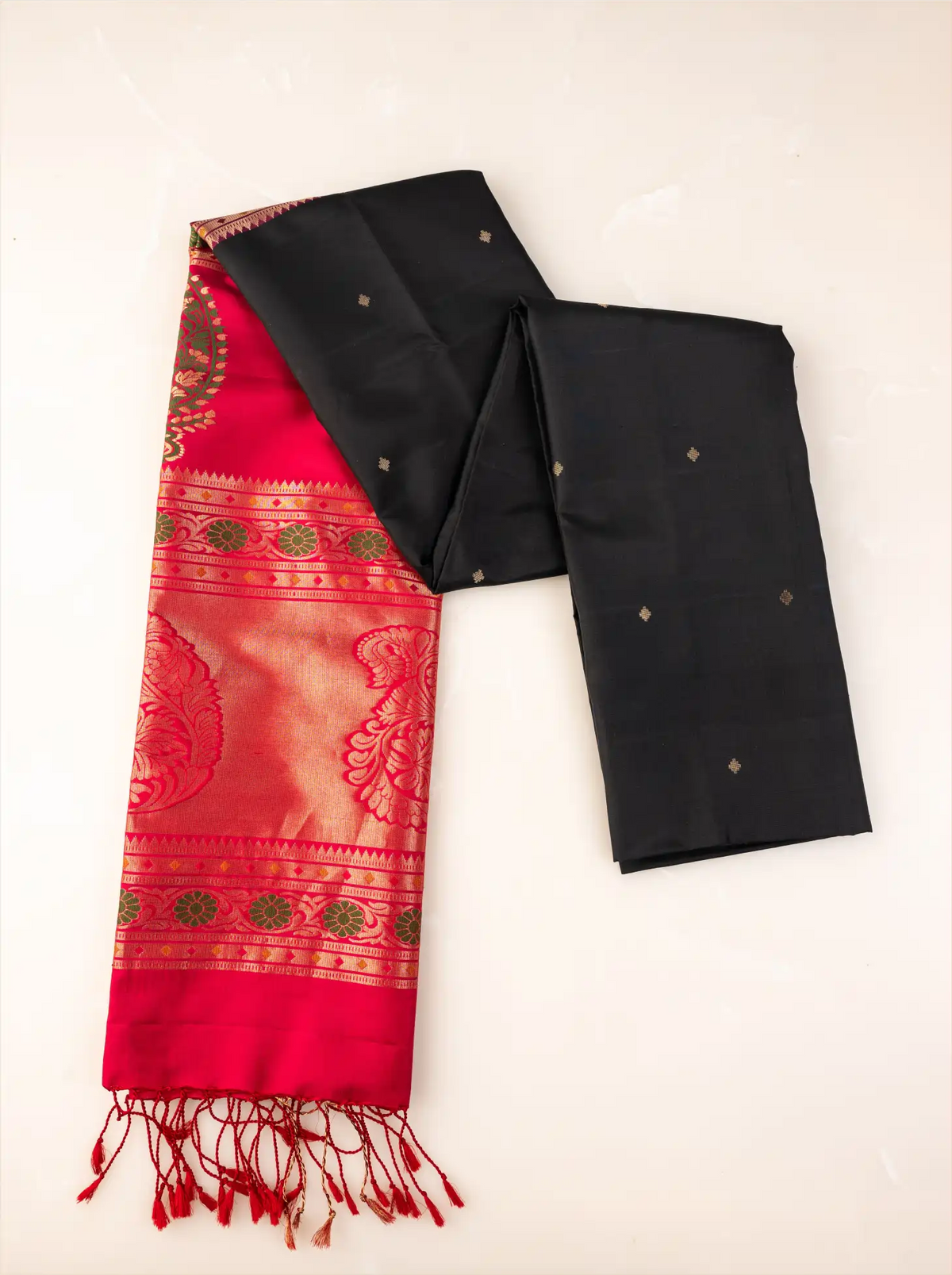 Handwoven pure Paithani silk saree neatly folded to showcase its jet black body with gold zari buttis, juxtaposed against a rich crimson red pallu featuring traditional floral zari borders and finished with red tassels.