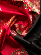 Close-up view of a handwoven pure Paithani silk saree featuring rich crimson red silk draped alongside black silk fabric, detailed with intricate gold zari woven borders and traditional green and red floral peacock pallu patterns.