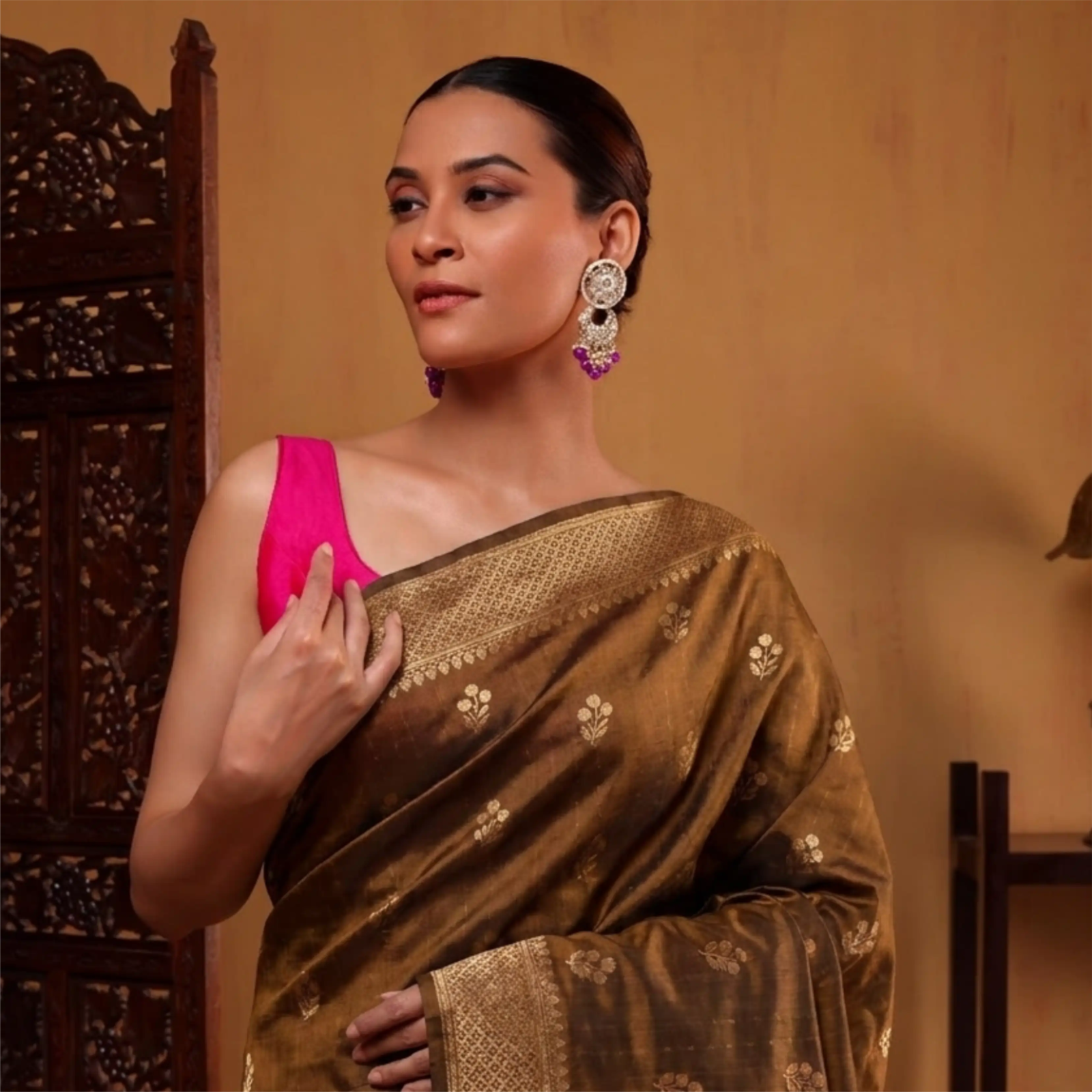 Model wearing a handcrafted earthy brown Alfi silk saree with gold zari floral motifs, paired with a vibrant pink sleeveless blouse.
