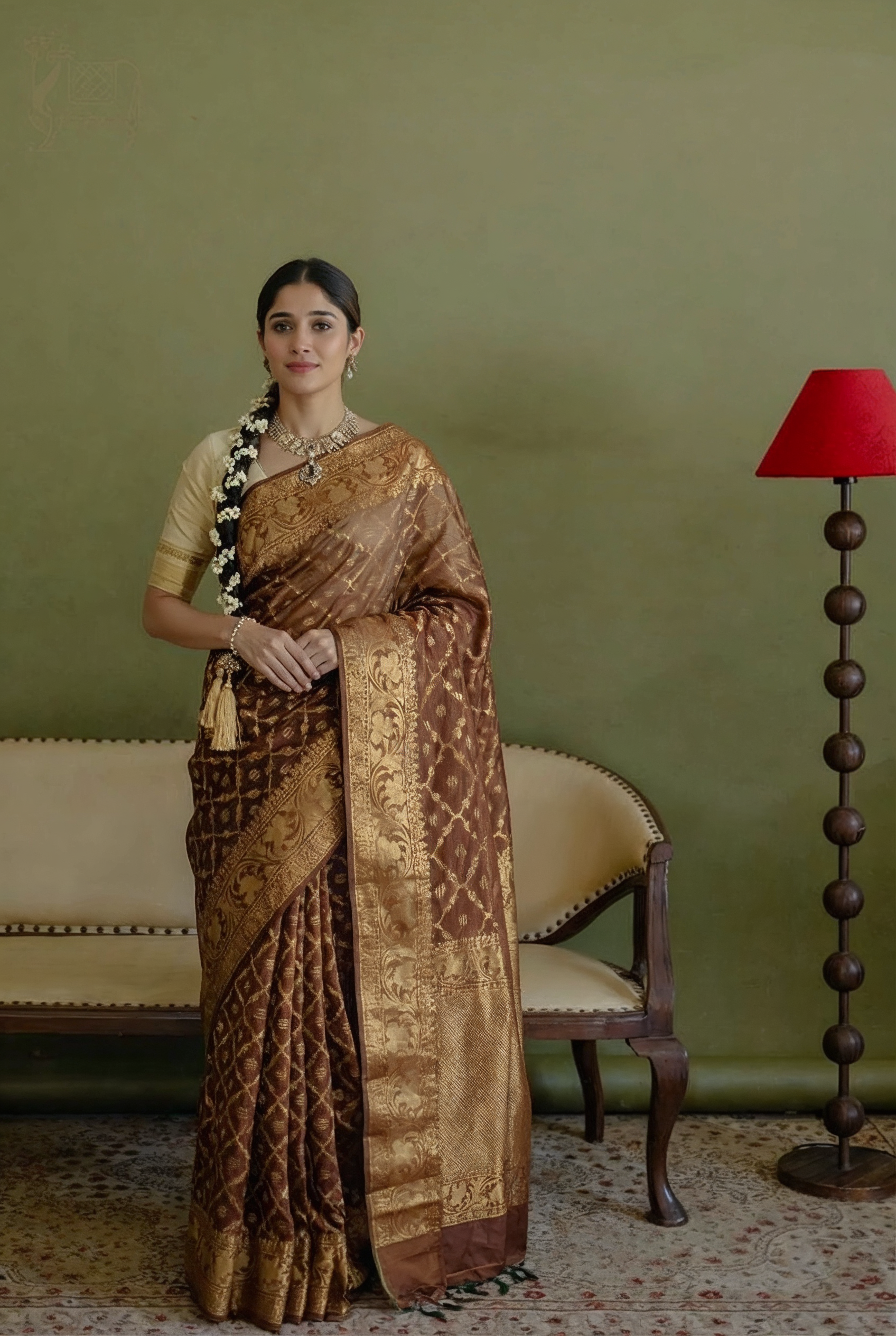 Woman wearing a handwoven earthy brown Jamdani silk cotton saree with intricate gold zari floral motifs and a traditional braid.