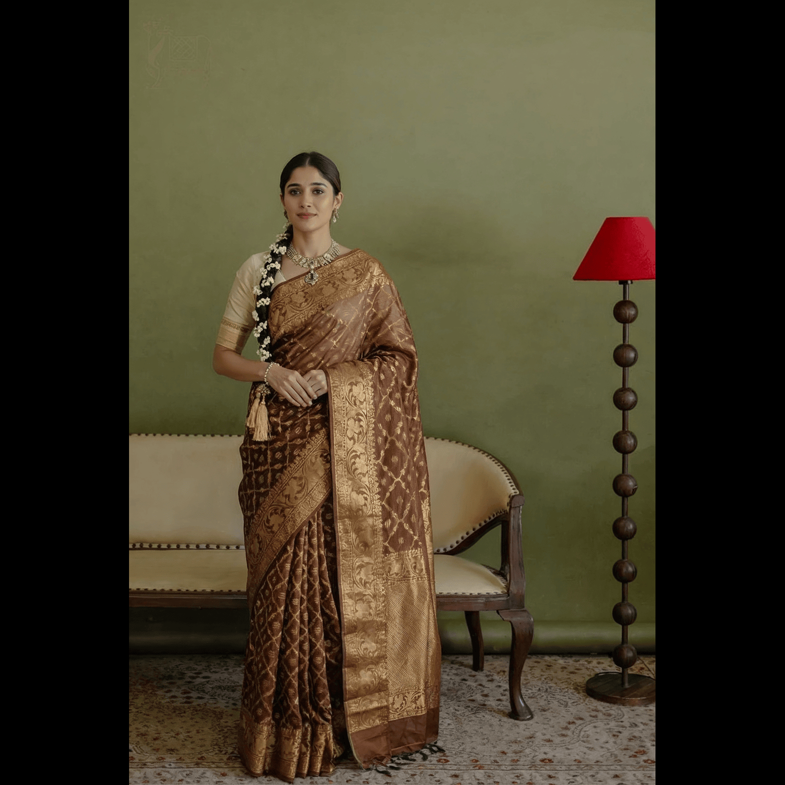 Woman wearing a handwoven earthy brown Jamdani silk cotton saree with intricate gold zari floral motifs and a traditional braid.