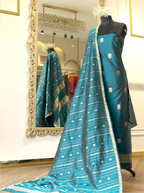 Teal blue handwoven Chinia silk suit set displayed on a mannequin, featuring gold zari floral bootis, a striped zari tissue dupatta with booti details, and a large ornate gold mirror in the background.
