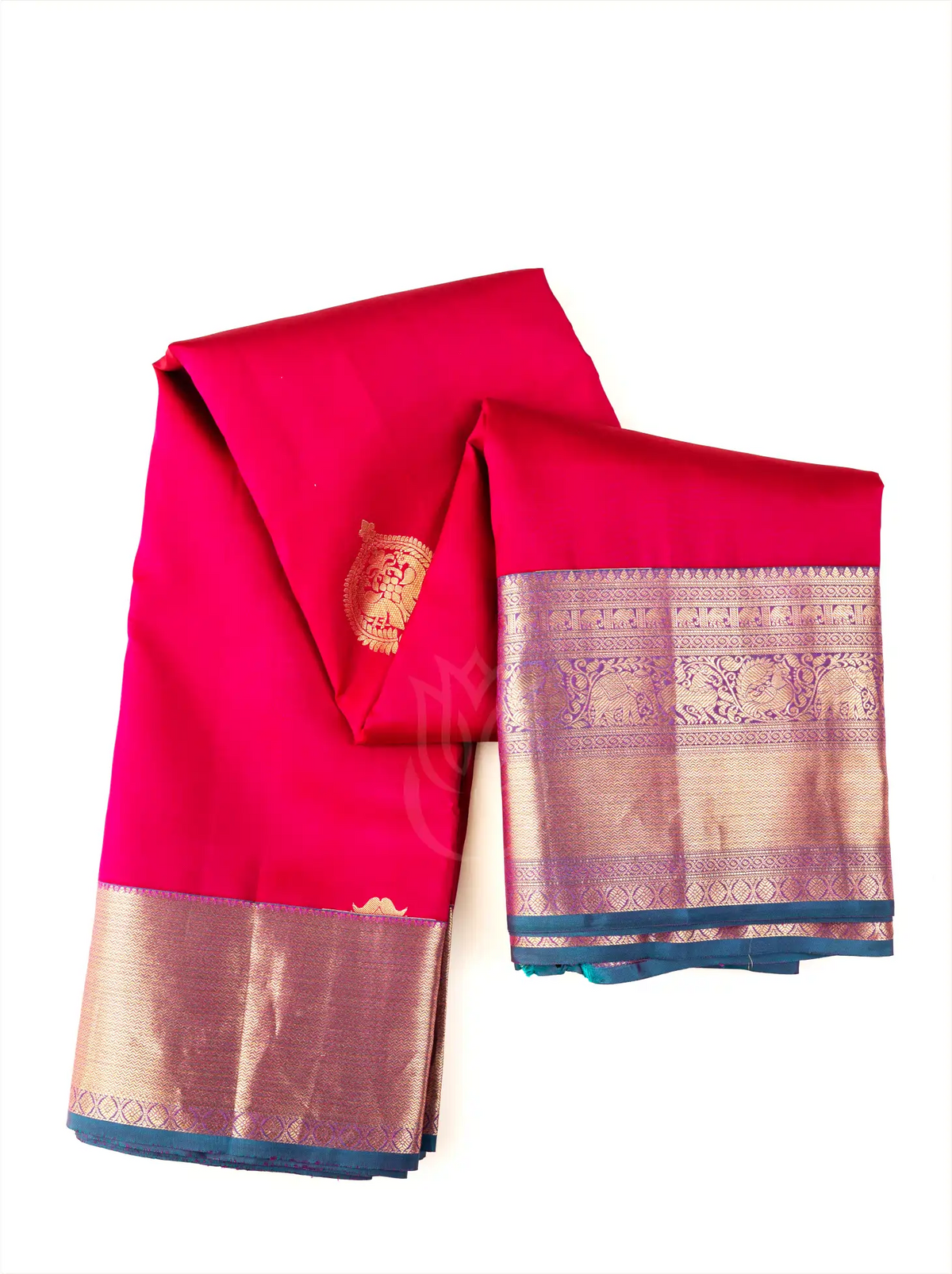 Folded handwoven crimson red pure Kanjivaram silk saree displayed against a clean white background, showcasing its gold zari motifs on the main body and an ornate deep teal pallu with gold brocade weaving.