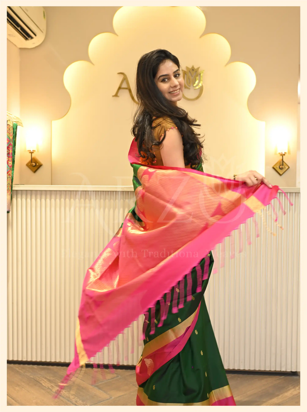 A woman wearing a handwoven dark green Mysore silk saree with a vibrant pink border and gold zari detailing.