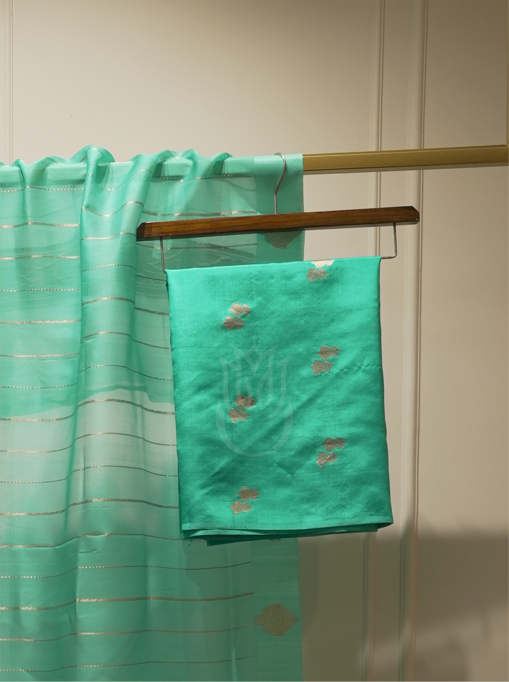 Seafoam green or emerald green handwoven silk suit fabric with gold and peach floral bootis folded on a wooden hanger, paired with a sheer gold-striped dupatta