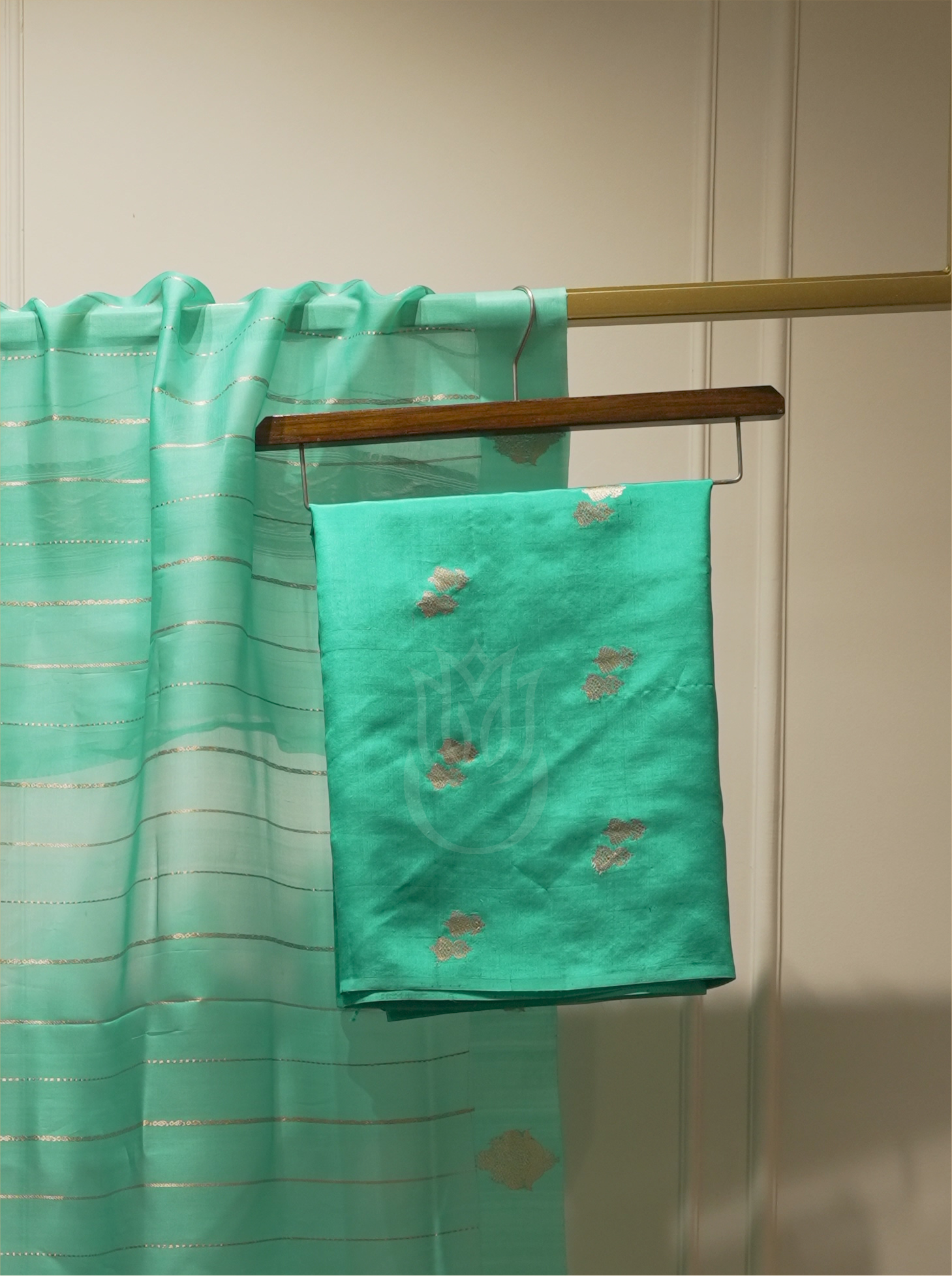 Seafoam green or emerald green handwoven silk suit fabric with gold and peach floral bootis folded on a wooden hanger, paired with a sheer gold-striped dupatta