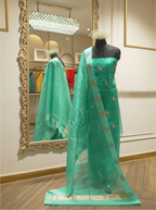Full-length display of an emerald green handwoven silk suit draped on a mannequin, styled with a sheer striped dupatta featuring woven zari borders and floral bootis, set near an ornate gold mirror