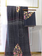 Handwoven pure georgette silk charcoal black suit fabric with gold micro bootis and a multi-color floral motif border draped on a stand next to a folded fabric piece.