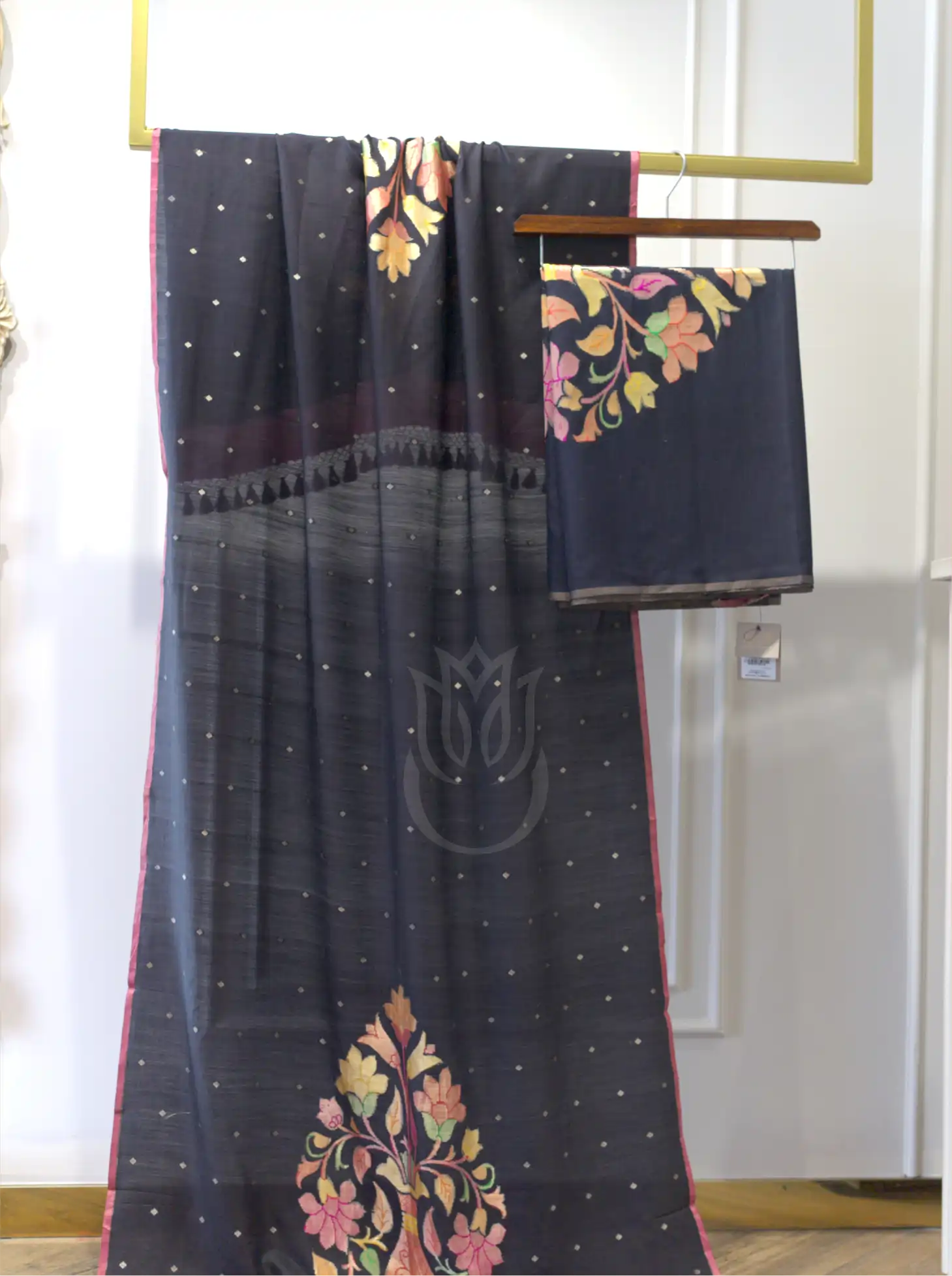 Handwoven pure georgette silk charcoal black suit fabric with gold micro bootis and a multi-color floral motif border draped on a stand next to a folded fabric piece.