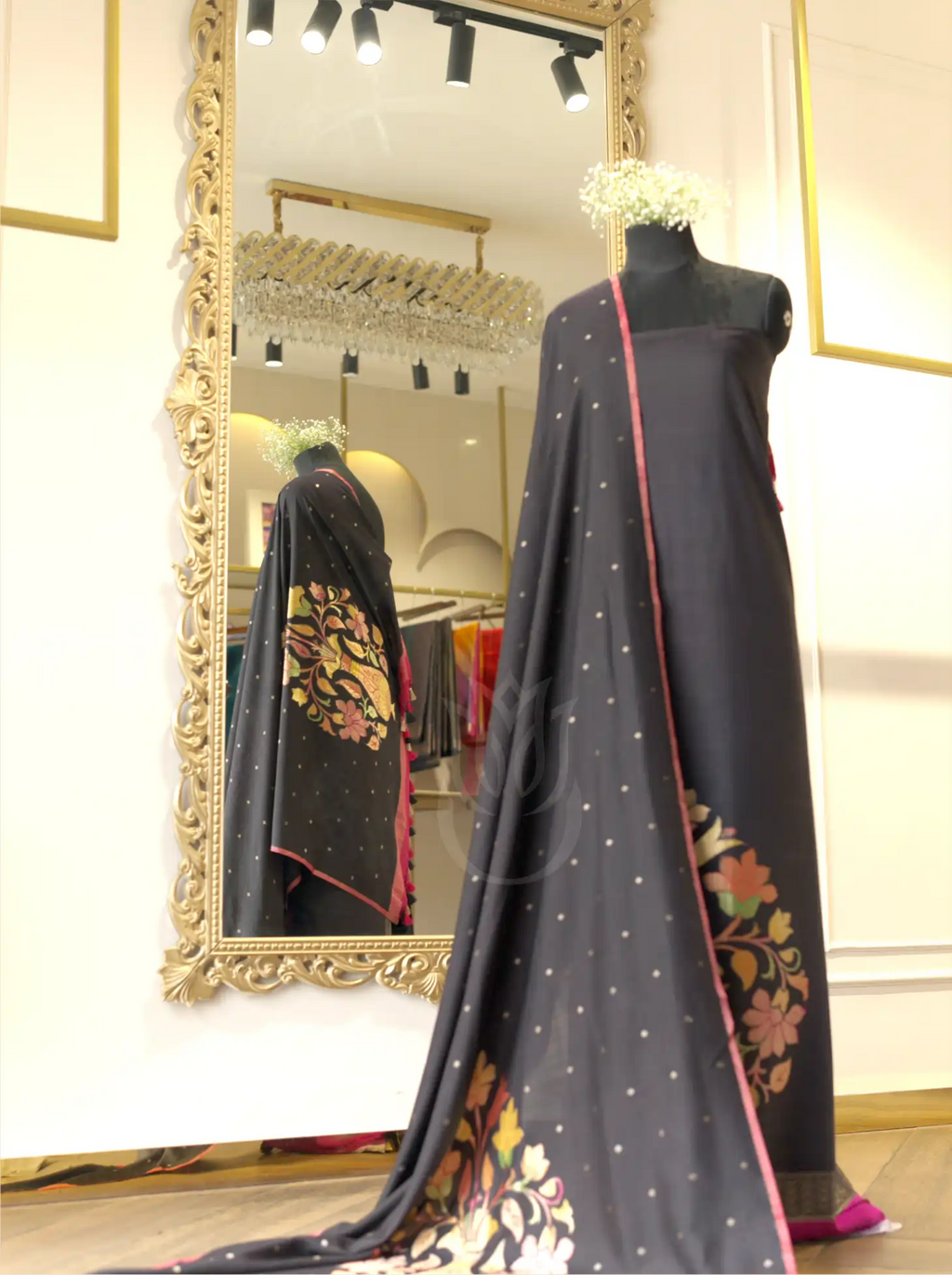 Handwoven pure georgette silk charcoal black suit fabric with gold micro bootis draped on a mannequin, featured alongside a matching dupatta with multi-color floral border motifs in a boutique setting.