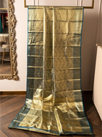 Handwoven metallic gold tissue Kanjivaram silk saree displayed vertically from a rack, showcasing its full pleated drape, rich metallic shimmer, dark teal zari border, and decorative lower pallu weave.