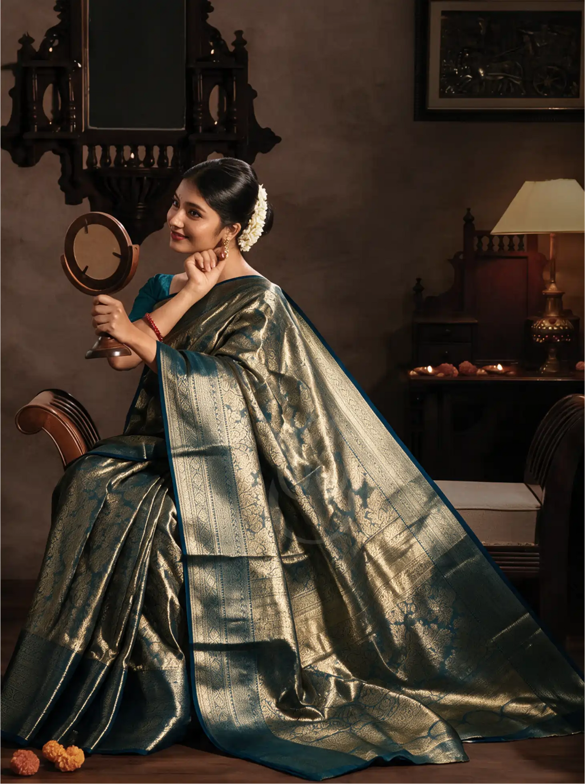 Model seated gracefully in traditional attire wearing a handwoven metallic gold tissue Kanjivaram silk saree, draped with a dark teal zari border and rich pallu.