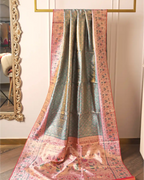 Handwoven green tissue Patola Kanjivaram silk saree with pink floral zari border draped on a gold display rack next to a decorative mirror.
