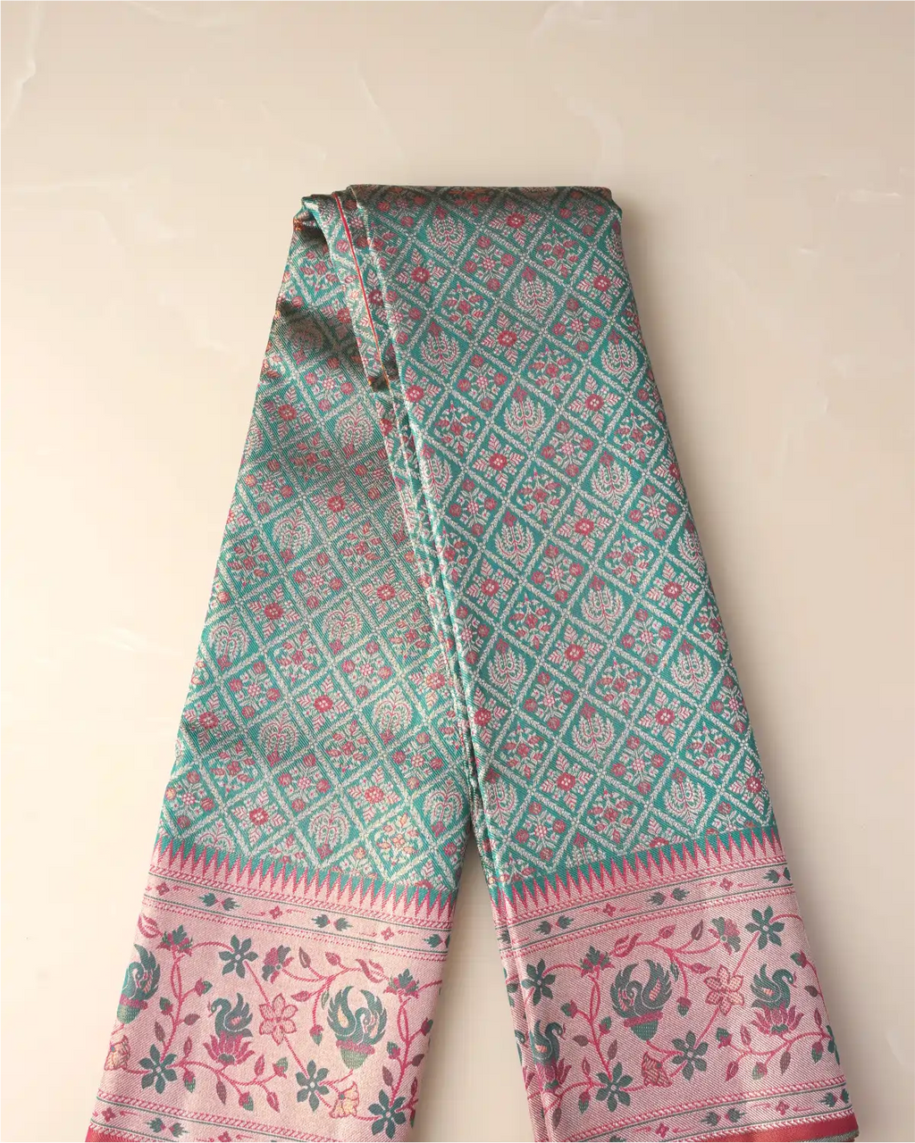 Folded length of a green tissue Patola Kanjivaram silk saree displaying geometric lattice patterns and a soft pink floral zari border.