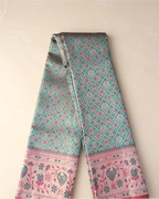 Folded length of a green tissue Patola Kanjivaram silk saree displaying geometric lattice patterns and a soft pink floral zari border.