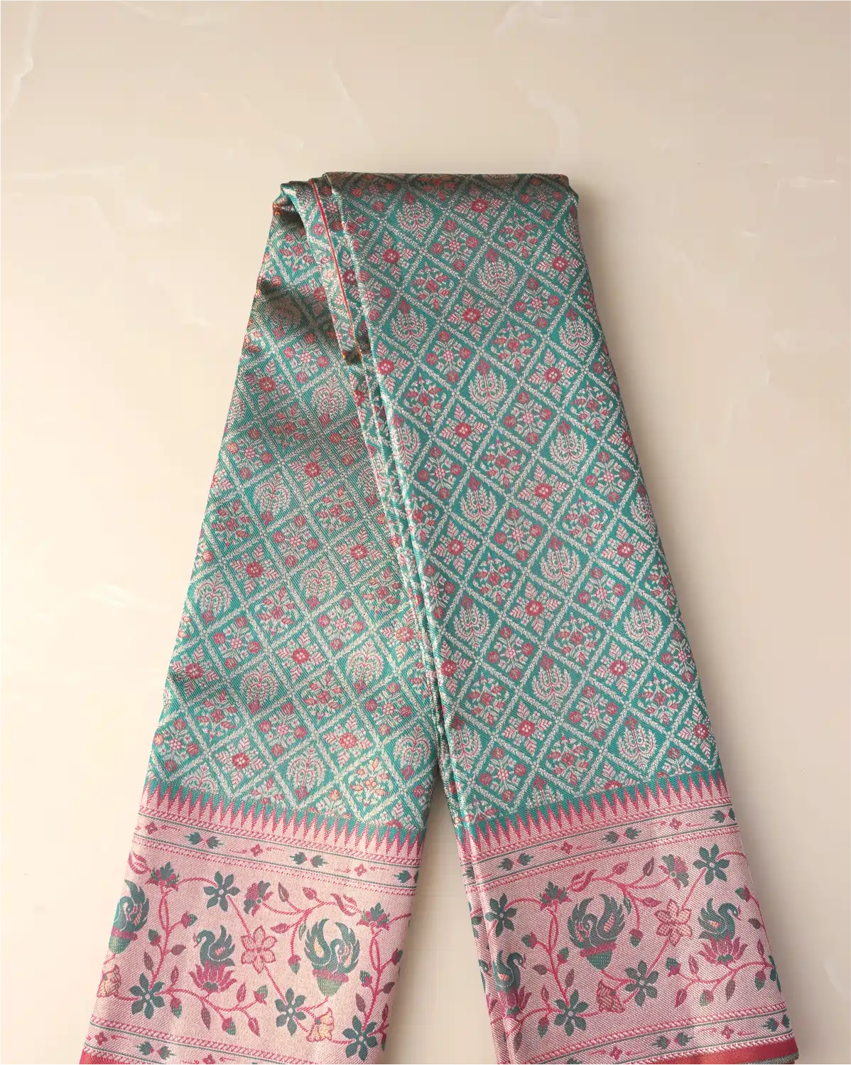 Folded length of a green tissue Patola Kanjivaram silk saree displaying geometric lattice patterns and a soft pink floral zari border.