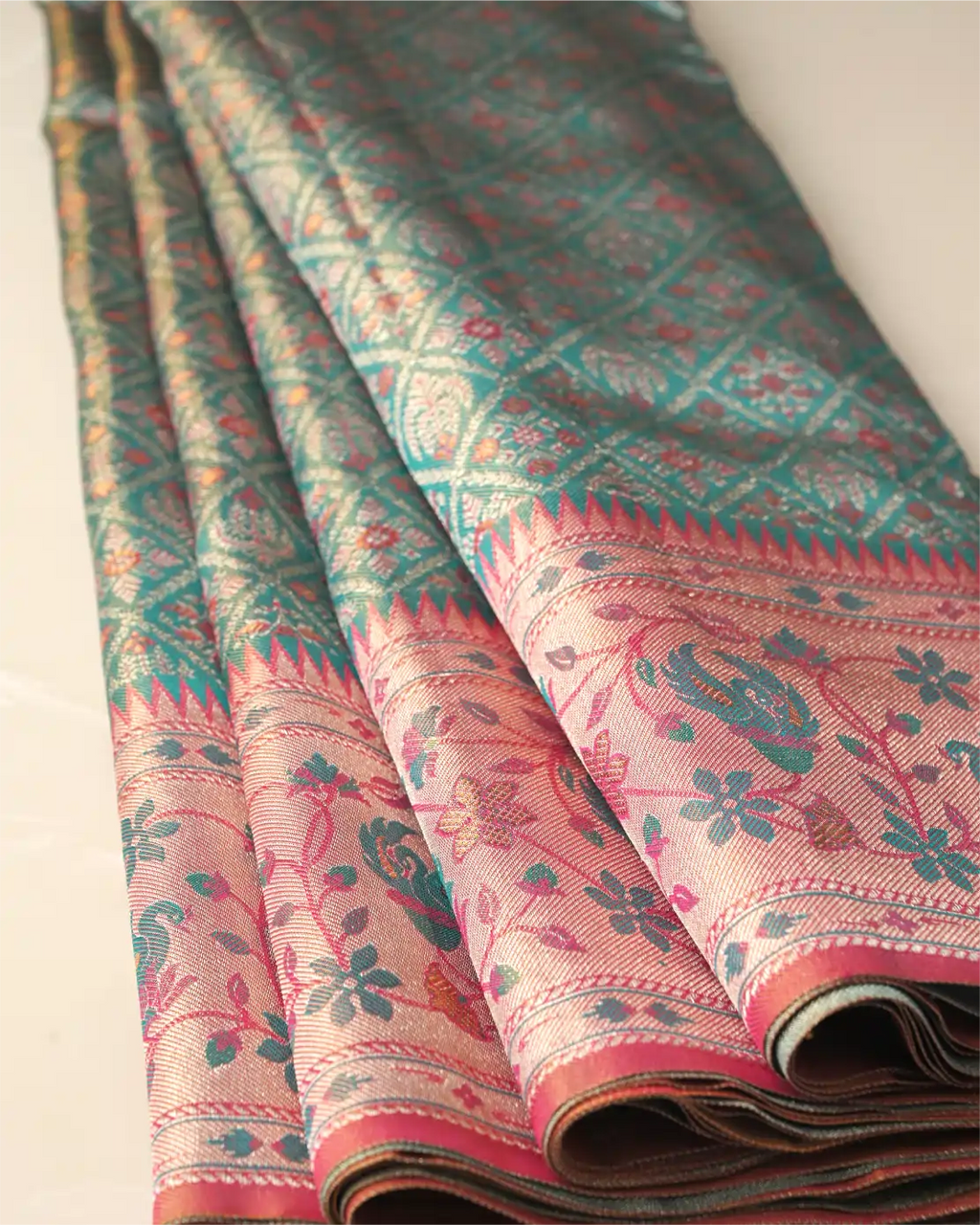 Folded sea green tissue Patola Kanjivaram silk saree showing intricate geometric lattice motifs and a pink floral zari border.