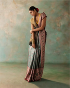 Woman wearing a handwoven green tissue Patola Kanjivaram silk saree with a pink zari floral border and gold blouse, posing in a studio.