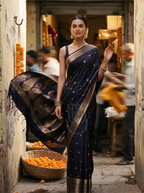 Model wearing a royal aubergine Kanjivaram Mysore silk saree featuring delicate gold zari bootis and a traditional woven zari pallu, paired with a dark sleeveless blouse and traditional gold jewelry.