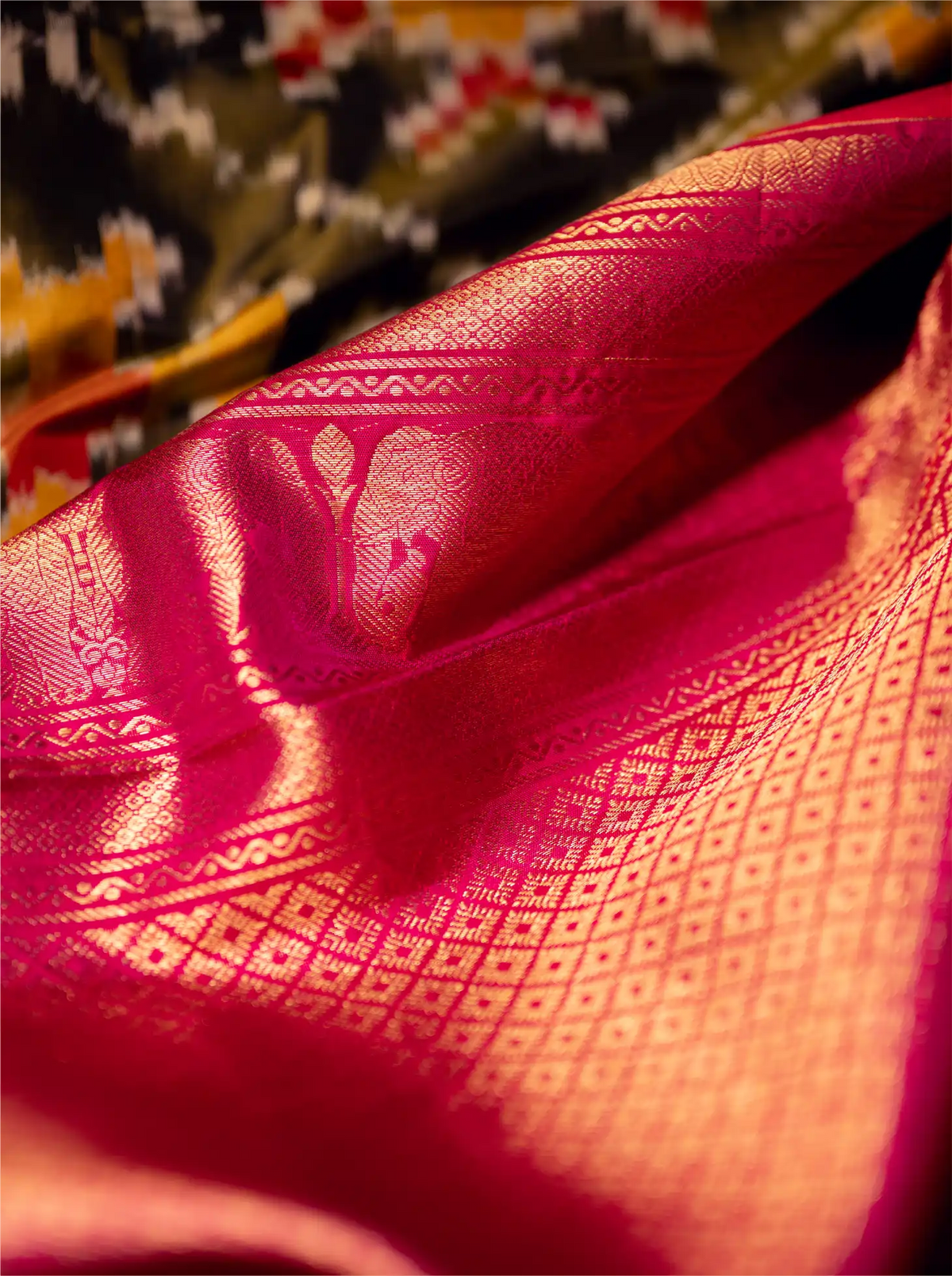 Close-up view of a handwoven Kanjivaram Patola silk saree showcasing a rich crimson red border with intricate gold zari woven geometric grid patterns.