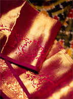 Close-up shot of a folded handwoven Kanjivaram Patola silk saree showcasing a rich crimson red pallu with elaborate gold zari floral motifs and a detailed woven border.