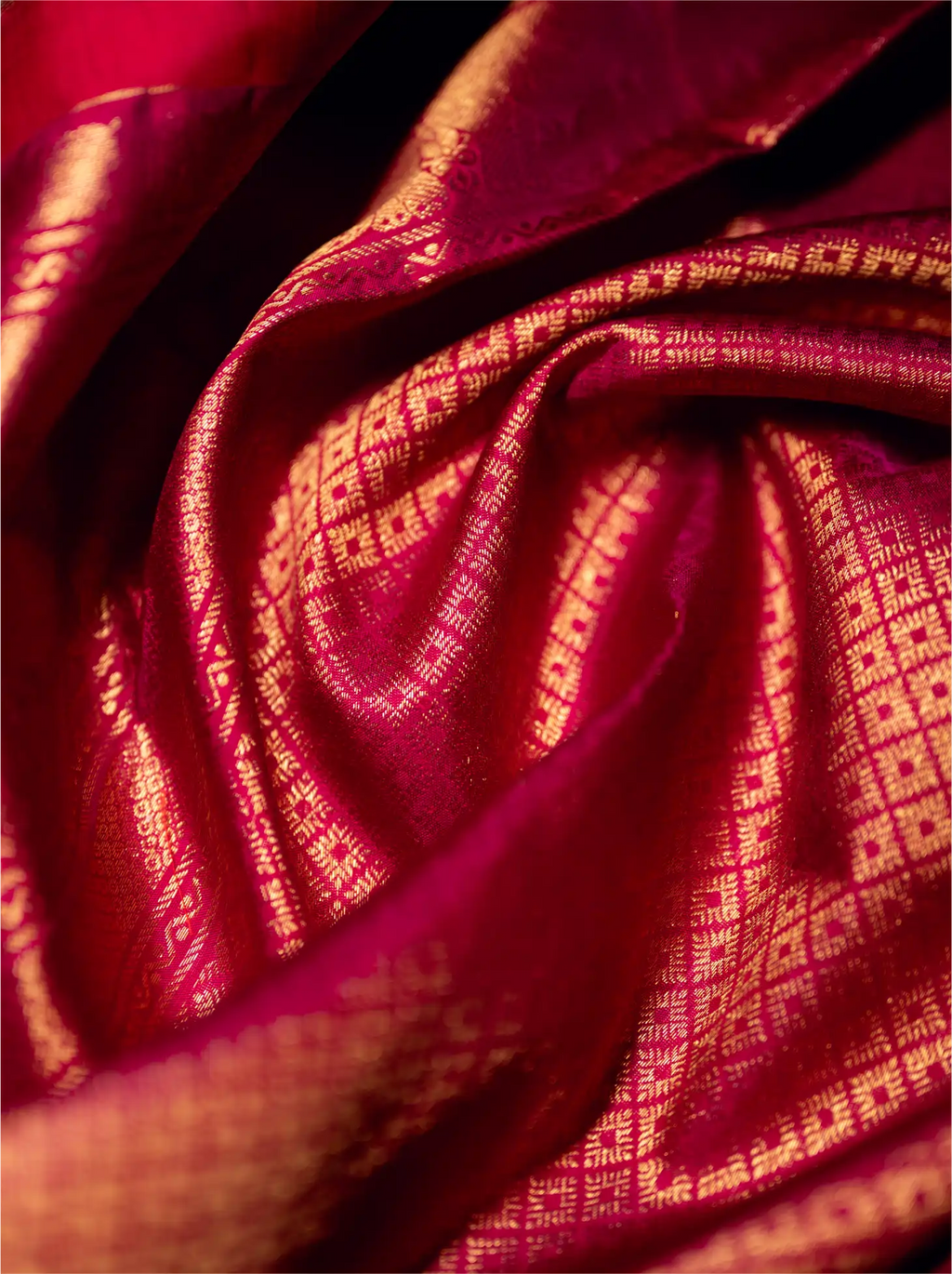 Close-up view of the folded crimson red handwoven Kanjivaram Patola silk saree showcasing rich metallic gold zari weaving with intricate square-grid brocade patterns.