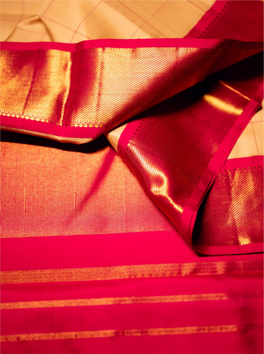 Close-up view of a handwoven crimson red Kanjivaram silk saree highlighting a luxurious gold zari border and rich metallic gold pallu drape with fine woven detailing.
