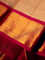 Close-up view of a folded handwoven Kanjivaram silk saree featuring a rich golden-yellow woven texture with fine grid lines and a contrasting deep magenta border adorned with intricate zari detailing.
